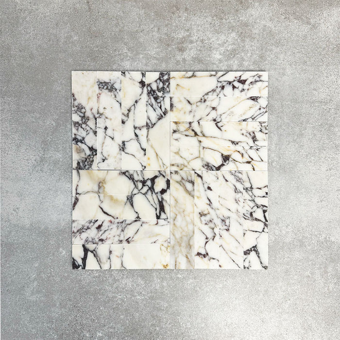 Arrangement featuring Fayrouz Picasso 5x20cm natural marble tiles with a honed finish, laid in a basketweave pattern to create visual texture and structure, showcasing a white base with bold grey, green and warm gold veining and natural variation across each piece.