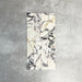Arrangement featuring Fayrouz Picasso 5x20cm natural marble tiles with a honed finish, displayed in a vertical layout to emphasise a white base with bold grey, green and warm gold veining, showcasing natural variation and flowing movement across each piece.