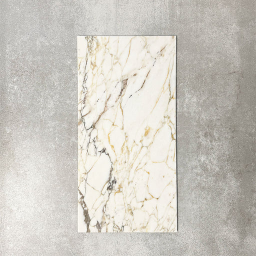 Fayrouz Picasso 30.5x61cm natural marble tiles with a honed finish, featuring a white base with intricate gold and grey veining, shown as a single tile sample against a neutral textured backdrop.