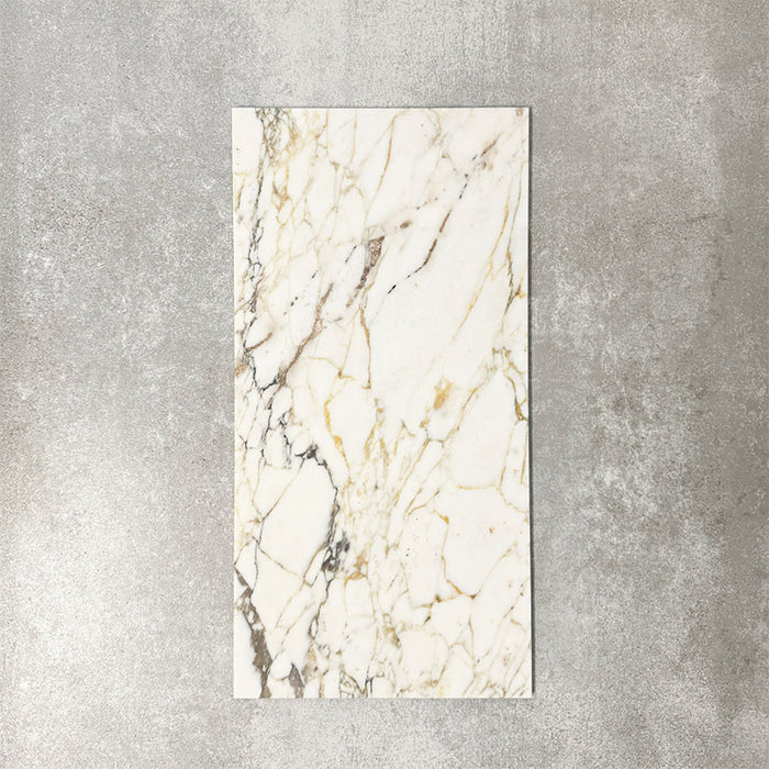 Fayrouz Picasso 30.5x61cm natural marble tiles with a honed finish, featuring a white base with intricate gold and grey veining, shown as a single tile sample against a neutral textured backdrop.