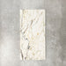 Fayrouz Picasso 30.5x61cm natural marble tiles with a honed finish, featuring a white base with intricate gold and grey veining, shown as a single tile sample against a neutral textured backdrop.