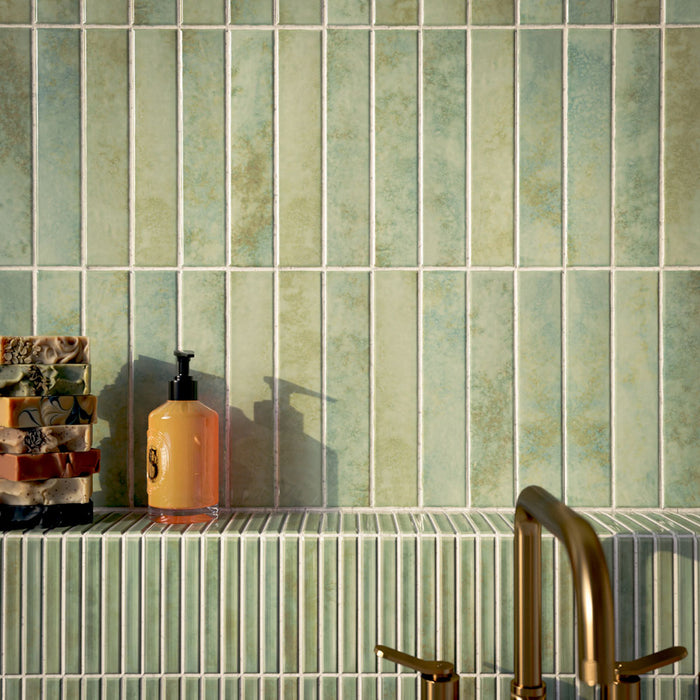 Bathroom featuring Pottery Agave Green 5x25cm glossy brick wall tiles with tonal variation, paired with striped tile detailing and brushed brass fixtures for a warm, spa-inspired contemporary interior.