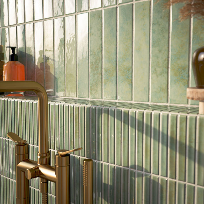 Bathroom featuring Pottery Agave Green 5x25cm glossy brick wall tiles with tonal variation, paired with striped tile detailing and brushed brass fixtures for a warm, spa-inspired contemporary interior.