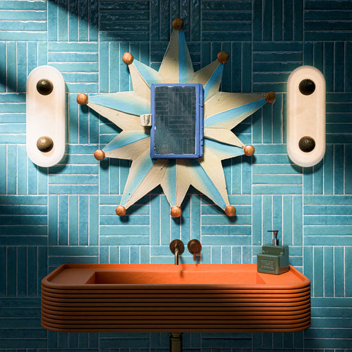 Bathroom featuring Pottery Azul Blue 5x25cm glossy brick wall tiles in a geometric layout, styled with a coral vanity unit, statement mirror, and brass fixtures for a bold contemporary interior.