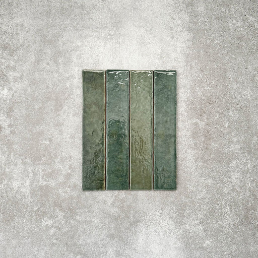 Product display of Pottery Brick Forest Green 5x25cm glossy wall tiles in rich forest green tones, featuring handcrafted edges and tonal variation against a textured concrete-style backdrop.
