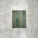 Product display of Pottery Brick Forest Green 5x25cm glossy wall tiles in rich forest green tones, featuring handcrafted edges and tonal variation against a textured concrete-style backdrop.