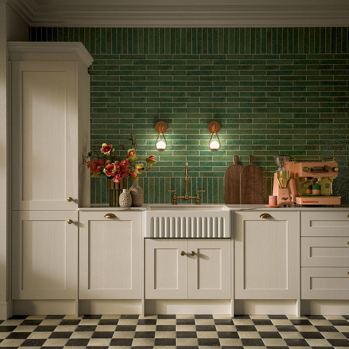 Kitchen featuring Pottery Forest Green 5x25cm glossy brick wall tiles, styled with cream shaker cabinetry, brass fixtures, a Belfast sink, and chequerboard floor tiles for a warm, vintage-inspired interior.