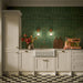 Kitchen featuring Pottery Forest Green 5x25cm glossy brick wall tiles, styled with cream shaker cabinetry, brass fixtures, a Belfast sink, and chequerboard floor tiles for a warm, vintage-inspired interior.