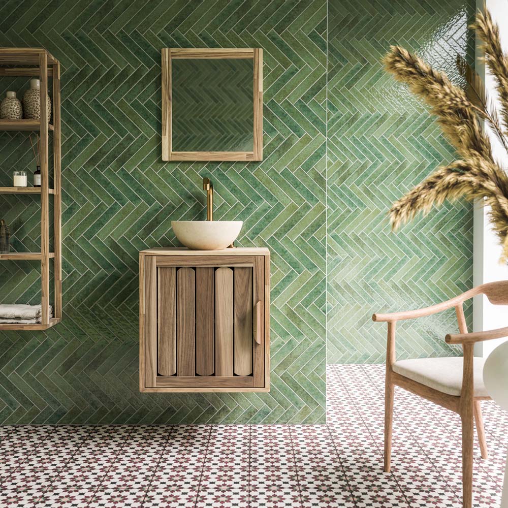 Contemporary bathroom featuring Pottery Forest Green Brick 5x25cm glossy wall tiles, arranged in a striking herringbone pattern, paired with burgundy and cream patterned floor tiles, natural wooden furniture, brass fittings and neutral accessories.