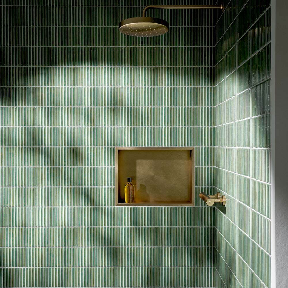 Walk-in shower featuring Pottery Decor Forest Green 12.5 × 25cm ceramic wall tiles, showcasing a rich glossy green finish with a vertically lined textured surface, paired with brass shower fittings and a recessed niche for a refined spa-inspired look.