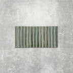 Product display of Pottery Decor Forest Green 12.5x25cm ceramic wall tiles in deep green tones, featuring a linear fluted design, handcrafted glossy finish and subtle tonal variation for textured contemporary interiors.