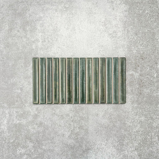 Product display of Pottery Decor Forest Green 12.5x25cm ceramic wall tiles in deep green tones, featuring a linear fluted design, handcrafted glossy finish and subtle tonal variation for textured contemporary interiors.