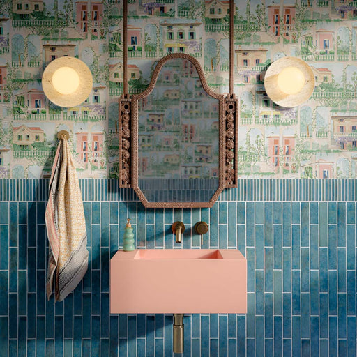 Bathroom featuring Pottery Prussian 5x25cm glossy brick wall tiles, styled with patterned wallpaper, a blush pink basin, and vintage-inspired brass fixtures for a bold, eclectic interior design.