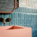 Bathroom featuring Pottery Prussian 5x25cm glossy brick wall tiles, styled with patterned wallpaper, a blush pink basin, and vintage-inspired brass fixtures for a bold, eclectic interior design.