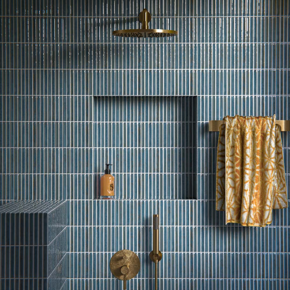 Shower interior featuring Pottery Decor Prussian wall tiles 12.5 × 25cm, laid in a vertical stacked layout to emphasise height and rhythm. The deep blue glazed finish with subtle tonal variation adds richness and depth, complemented by a built-in niche, ribbed tiled bench, and brushed brass fittings for a refined, contemporary look.