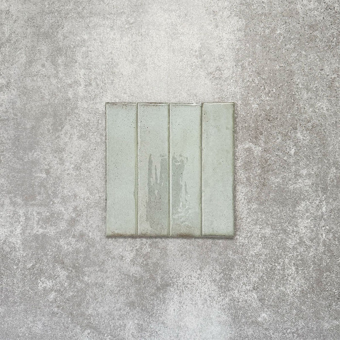 Product image of Puzzle Breeze Green Brick Rectified 5x20cm wall and floor tiles, featuring a glossy pale green finish with subtle tonal variation and softly aged edges, displayed to highlight the tile's handcrafted character.