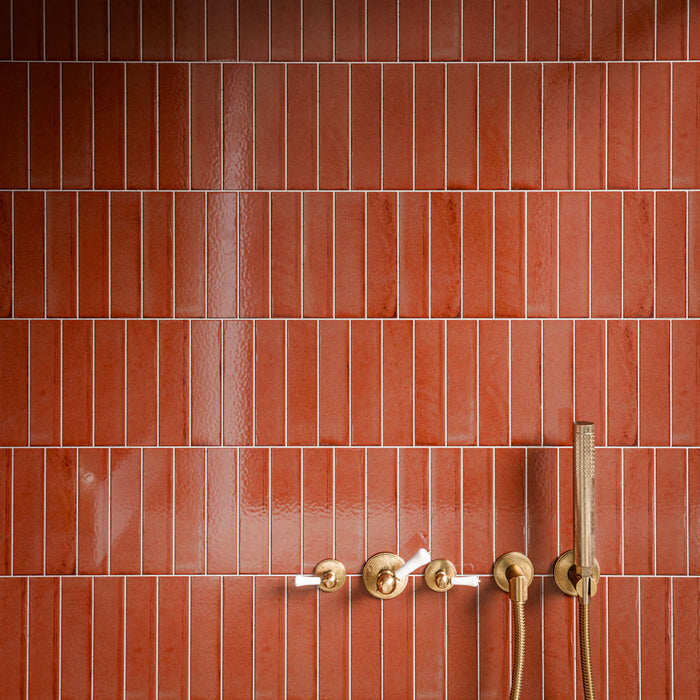 Close-up of Puzzle Coral Brick Rectified 5cm x 20cm tiles across a shower wall, showcasing warm coral tones and subtle surface variation, paired with brushed brass shower controls and fixtures.