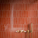 Close-up of Puzzle Coral Brick Rectified 5cm x 20cm tiles across a shower wall, showcasing warm coral tones and subtle surface variation, paired with brushed brass shower controls and fixtures.