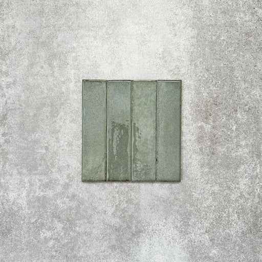 Product image of Puzzle Sage Green Brick Rectified 5x20cm wall and floor tiles, featuring a glossy sage green finish with subtle tonal variation and softly aged edges, displayed to highlight the tile's handcrafted character.