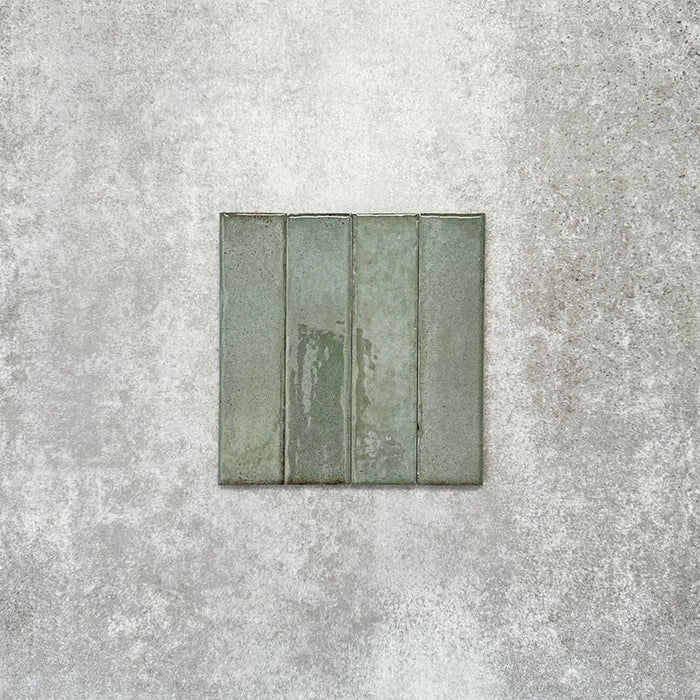 Product image of Puzzle Sage Green Brick Rectified 5x20cm wall and floor tiles, featuring a glossy sage green finish with subtle tonal variation and softly aged edges, displayed to highlight the tile's handcrafted character.