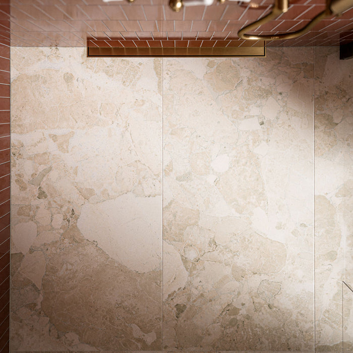 Close-up of Riad Avorio Sassi Terrazzo Stone 60cm x 120cm tiles across a shower wall, showcasing a warm ivory stone effect with varied natural-looking fragments and subtle tonal variation, paired with coral brick tiles and brass details.