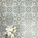 Group of London Streets Regent Street 20x20cm Victorian Moroccan style porcelain tiles arranged to showcase the repeating green, sage and cream floral geometric pattern, styled with white flowers in a decorative flat-lay setting.