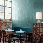 Restaurant interior featuring Nomad Aquamarine brick wall tiles in a 6 × 24.6cm format, laid vertically to create a rich teal feature wall with an industrial-style feel.