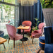 Restaurant seating area featuring London Streets Carnegie Hall 20x20cm Victorian Moroccan style floor tiles, styled with pink upholstered chairs, wooden tables, navy curtains and large windows creating a colourful patterned café interior.
