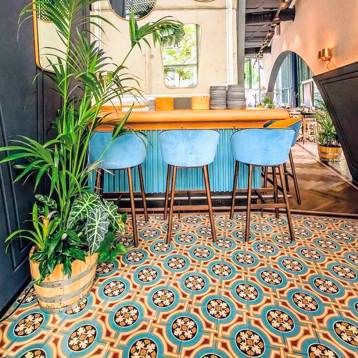 Restaurant seating area featuring London Streets Carnegie Hall 20x20cm Victorian Moroccan style floor tiles, styled with pink upholstered chairs, wooden tables, navy curtains and large windows creating a colourful patterned café interior.