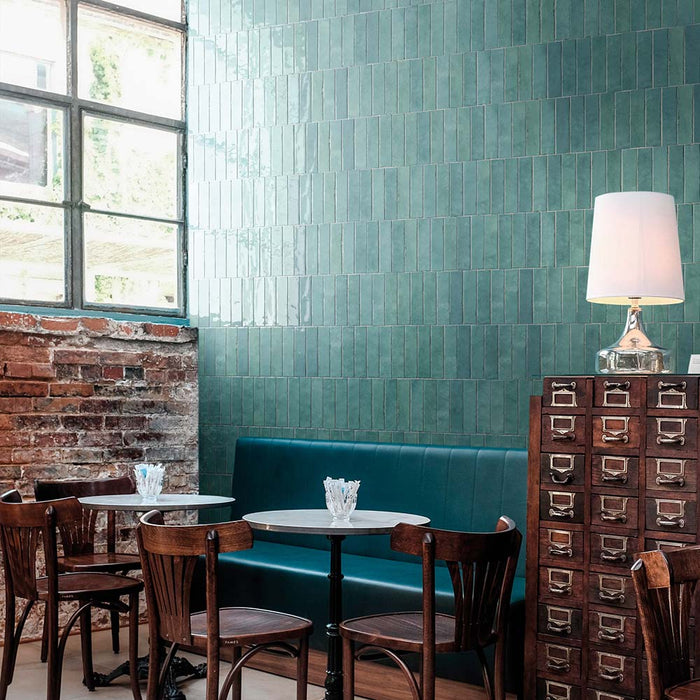 Restaurant interior featuring Nomad Aquamarine brick wall tiles in a 6 × 24.6cm format, laid vertically to create a rich teal feature wall with an industrial-style feel.