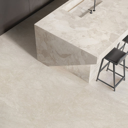 Contemporary kitchen featuring Riad Avorio Neutra Stone 30x60cm stone-effect wall and floor tiles, showcasing warm ivory and beige tones, paired with a matching waterfall island, black bar stools and minimalist finishes.