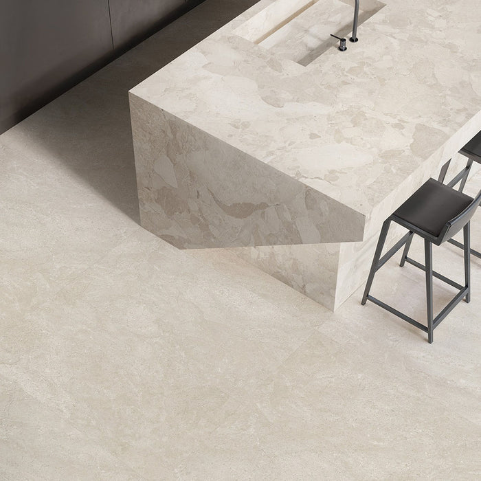 Contemporary kitchen featuring Riad Avorio Neutra Stone 30x60cm stone-effect wall and floor tiles, showcasing warm ivory and beige tones, paired with a matching waterfall island, black bar stools and minimalist finishes.