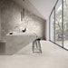 Contemporary kitchen featuring Riad Avorio Neutra Stone 30x60cm stone-effect wall and floor tiles, showcasing warm ivory and beige tones, paired with a matching waterfall island, black bar stools and minimalist finishes.