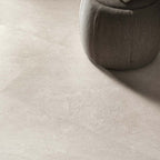Close-up of Riad Avorio Neutra Stone 30x60cm stone-effect floor tiles, showcasing warm ivory and beige tones with delicate natural stone-inspired veining, paired with a soft upholstered pouffe in a contemporary interior.