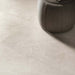 Close-up of Riad Avorio Neutra Stone 30x60cm stone-effect floor tiles, showcasing warm ivory and beige tones with delicate natural stone-inspired veining, paired with a soft upholstered pouffe in a contemporary interior.