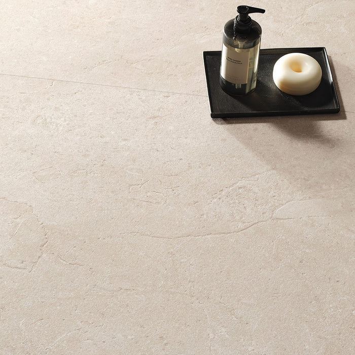 Close-up of Riad Avorio Neutra Stone 60x60cm stone-effect floor tiles, showcasing warm ivory and beige tones with delicate natural stone-inspired veining, styled with a black tray, soap dispenser and minimalist bathroom accessories.