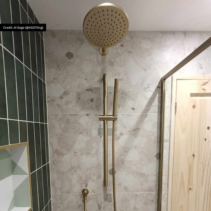 Customer bathroom featuring Riad Avorio Sassi Stone 30x60cm stone-effect wall tiles, showcasing warm ivory and beige tones with natural stone-inspired detailing, paired with brushed brass shower fittings and deep green brick tiles.