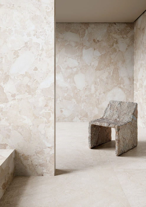 Interior featuring Riad Blanco Neutra Stone 30x60cm stone-effect wall and floor tiles, showcasing soft cream and beige tones with natural stone-inspired detailing, paired with a sculptural stone chair in a minimalist contemporary space.