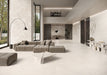 Contemporary living space featuring Riad Blanco Neutra Stone 30x60cm stone-effect wall and floor tiles, showcasing soft cream and beige tones, paired with minimalist furniture, floor-to-ceiling glazing and warm natural textures.