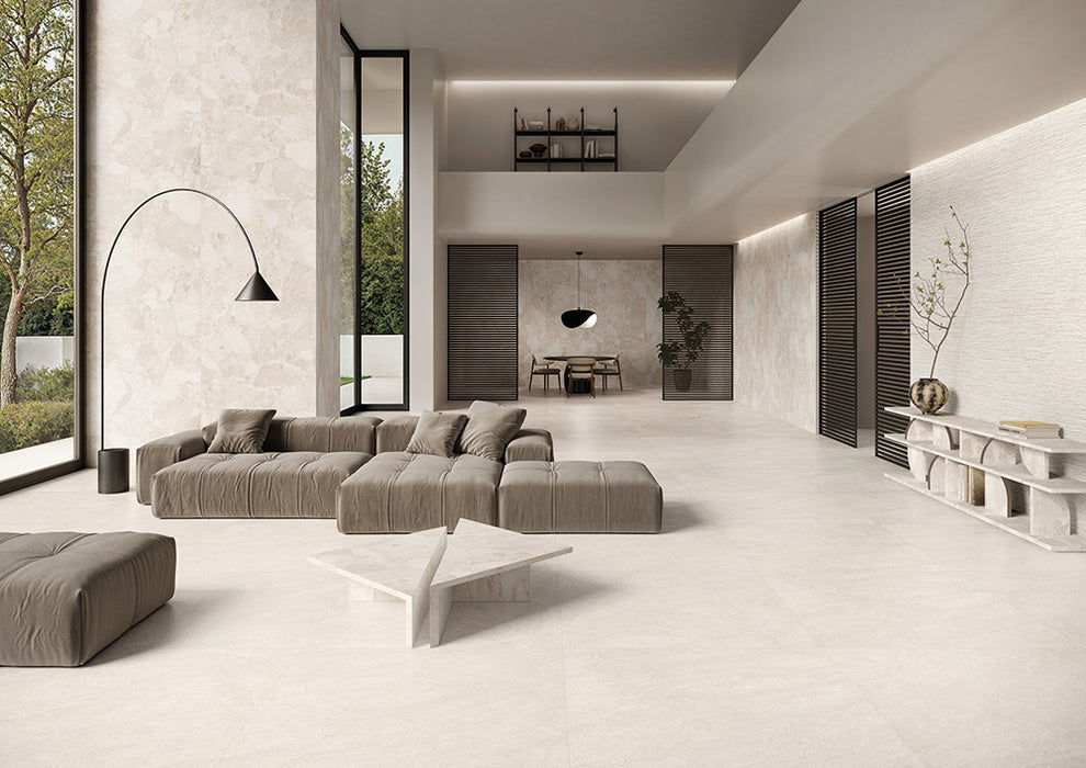 Contemporary living space featuring Riad Blanco Neutra Stone 30x60cm stone-effect wall and floor tiles, showcasing soft cream and beige tones, paired with minimalist furniture, floor-to-ceiling glazing and warm natural textures.