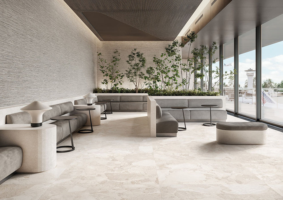 Contemporary lounge featuring Riad Blanco Sassi Terrazzo Stone 60x120cm stone-effect floor tiles, showcasing soft cream and beige tones with natural stone-inspired detailing, paired with minimalist seating, indoor planting and floor-to-ceiling glazing.