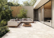 Contemporary outdoor patio featuring Riad Blanco Terrazzo 20mm 100x100cm outdoor stone-effect porcelain tile slabs, showcasing soft cream and beige tones, paired with minimalist lounge seating, timber furniture and landscaped gardens.