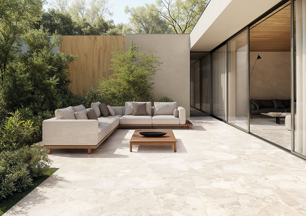 Contemporary outdoor patio featuring Riad Blanco Terrazzo 20mm 100x100cm outdoor stone-effect porcelain tile slabs, showcasing soft cream and beige tones, paired with minimalist lounge seating, timber furniture and landscaped gardens.