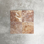 Four Fayrouz Rosso 15.2x15.2cm natural marble tiles with a tumbled finish arranged together, showcasing warm red tones, distinctive veining and natural variation against a neutral textured background.