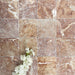 Flat lay of Fayrouz Rosso 15.2x15.2cm natural marble tiles with a tumbled finish, featuring warm red tones, natural veining and surface variation, styled with soft white flowers for contrast.