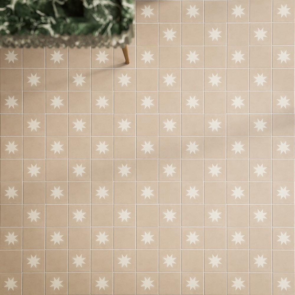 Close-up of Rubins Gold Base MINI 15x15cm Moroccan-style porcelain floor tiles, featuring warm sandy beige tones in a square grid layout, paired with white star-patterned decor tiles, natural greenery and brass accents.