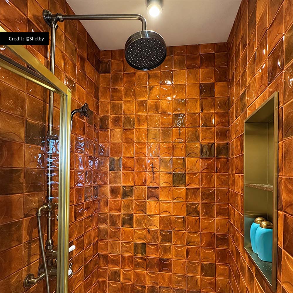 Customer shower featuring Saigon Amber Decor Square 10x10cm Moroccan-style wall tiles, with rich amber and burnt orange tones, a glossy textured finish and raised geometric detailing, paired with brass shower fittings.