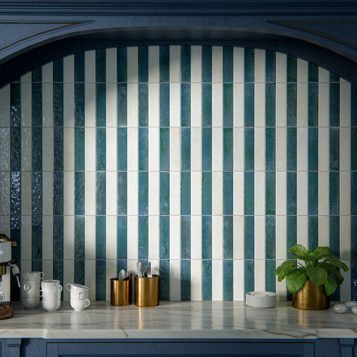 Kitchen interior featuring Allegra Blanca 6x25cm gloss brick tiles, installed vertically within a statement alcove, showcasing soft white tones with a reflective glazed finish, styled with deep blue cabinetry, brass accents, and a marble-effect worktop for a refined, elegant contrast.