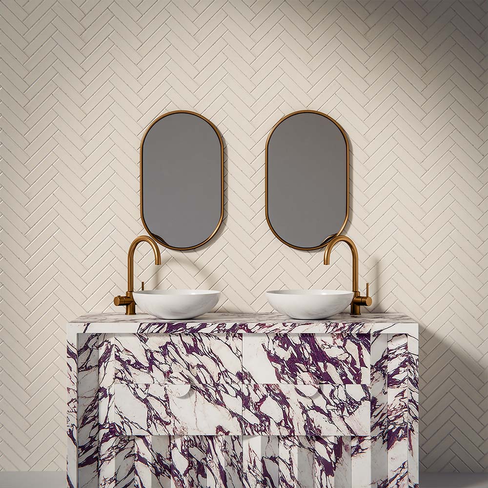 Puzzle White Brick Rectified 5x20cm porcelain tiles styled in a classic herringbone layout, creating a clean and timeless bathroom backdrop. The soft white tone and subtle surface variation add gentle depth while maintaining a crisp, contemporary feel. Paired with brushed brass fittings and a bold marble-effect vanity, the slim brick format enhances texture and pattern, making it ideal for elegant bathroom walls or refined feature areas.