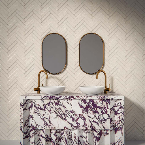 Puzzle White Brick Rectified 5x20cm porcelain tiles styled in a classic herringbone layout, creating a clean and timeless bathroom backdrop. The soft white tone and subtle surface variation add gentle depth while maintaining a crisp, contemporary feel. Paired with brushed brass fittings and a bold marble-effect vanity, the slim brick format enhances texture and pattern, making it ideal for elegant bathroom walls or refined feature areas.